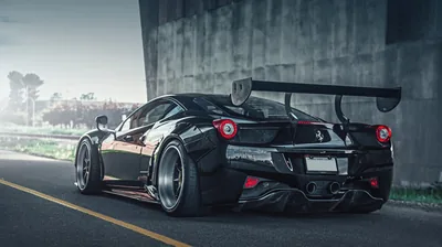 Rear three-quarter of a track-prepped 458 under a concrete underpass, its swan-neck wing and wide fenders framed by roadside grass and daylight beyond.