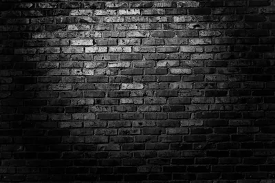 A hard cone of light lands on old brickwork from the upper left, the mortar bright and the outer edges left in monochrome shadow.
