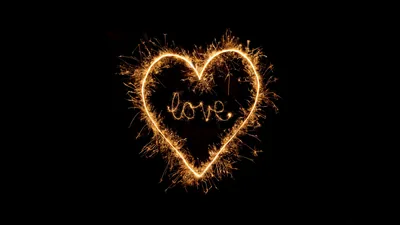 A heart drawn in burning sparkler trails on pure black, the word love written in the same gold script at its centre.