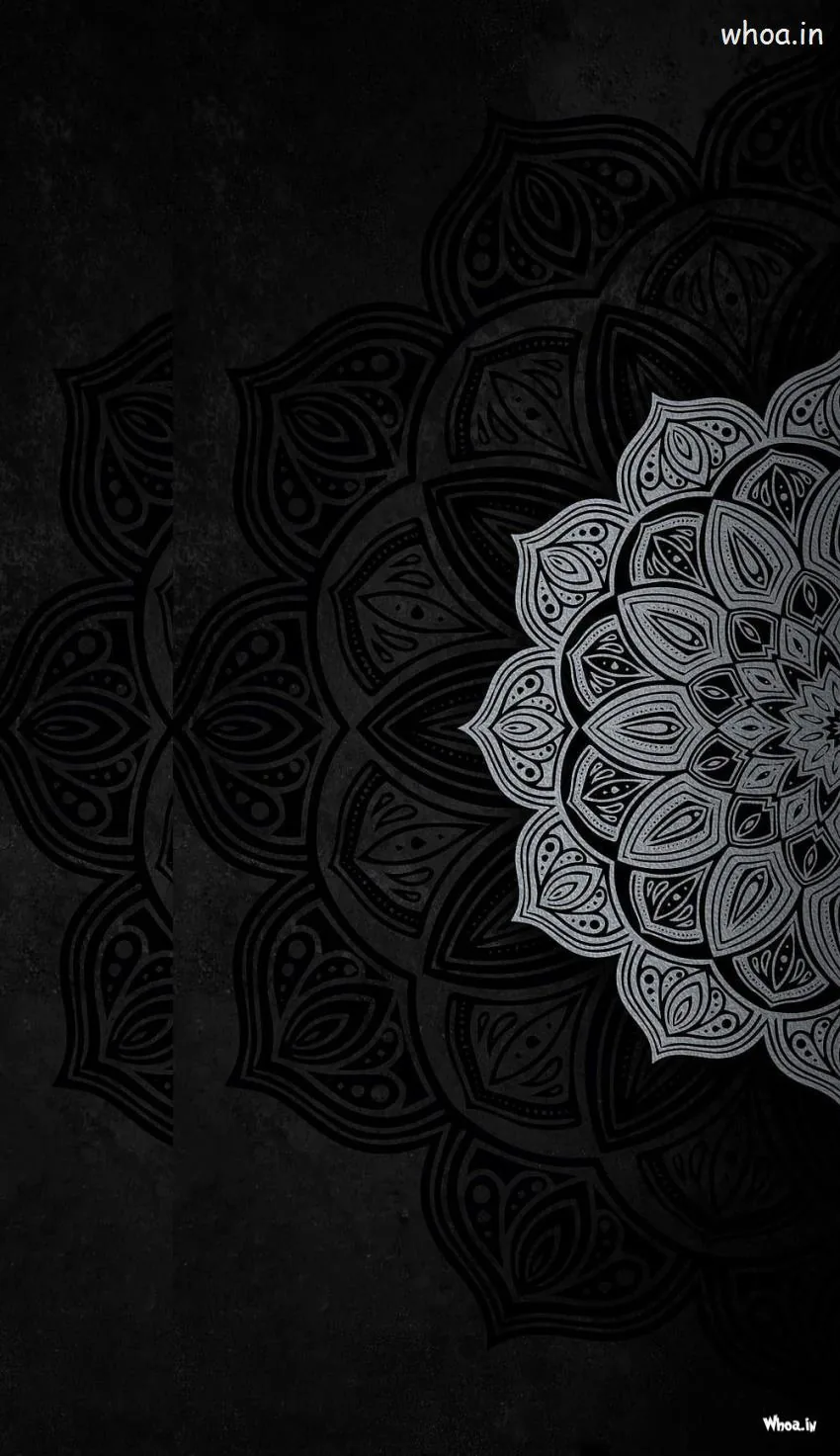 A half mandala in fine grey line work sits against a scuffed dark wall, its detail densest along the right edge.
