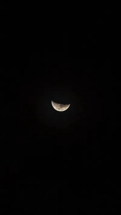 A lone half moon hangs low in an otherwise empty black sky — nearly the whole frame is true black, with the top clear for the clock.