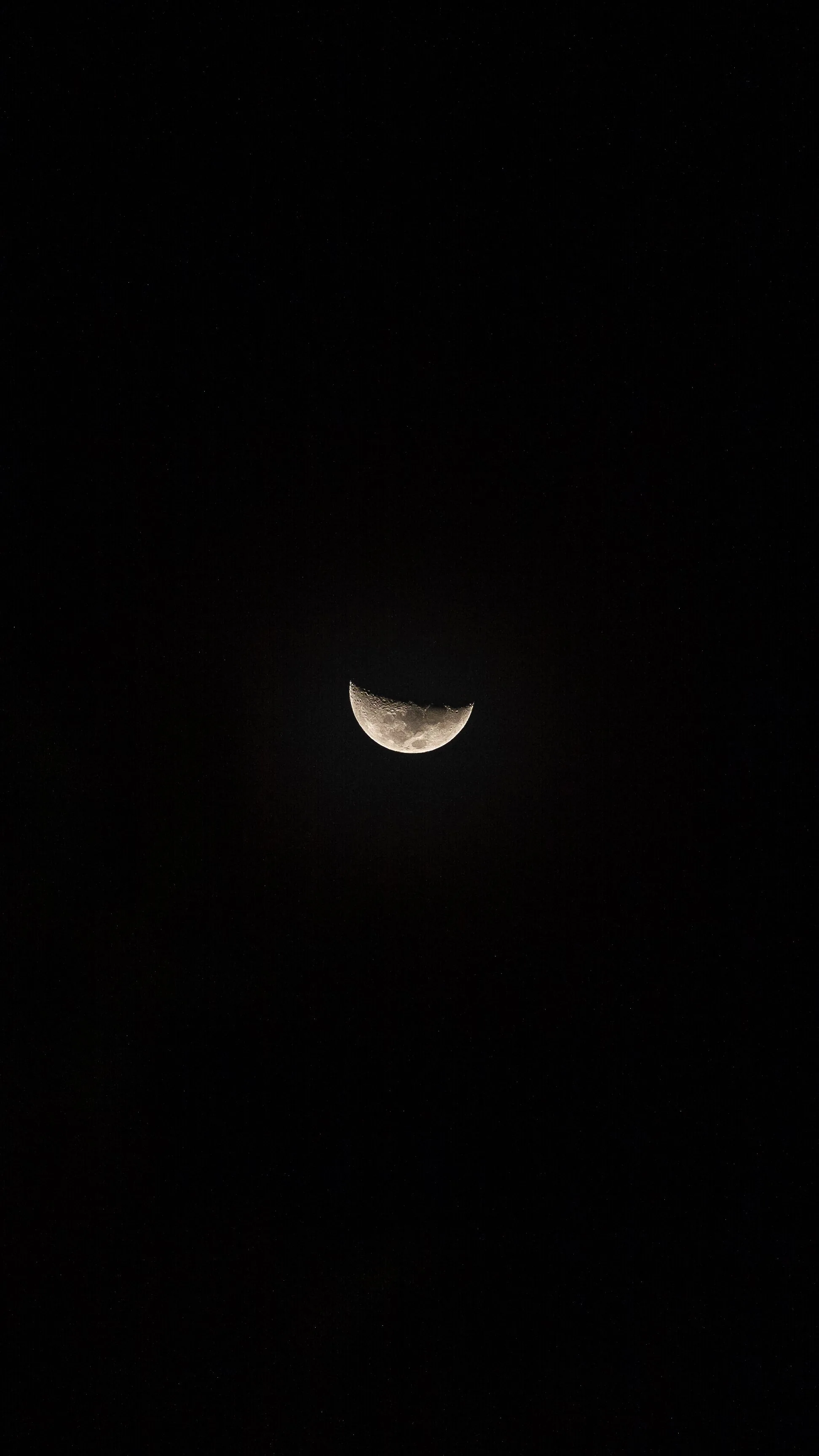 A lone half moon hangs low in an otherwise empty black sky — nearly the whole frame is true black, with the top clear for the clock.