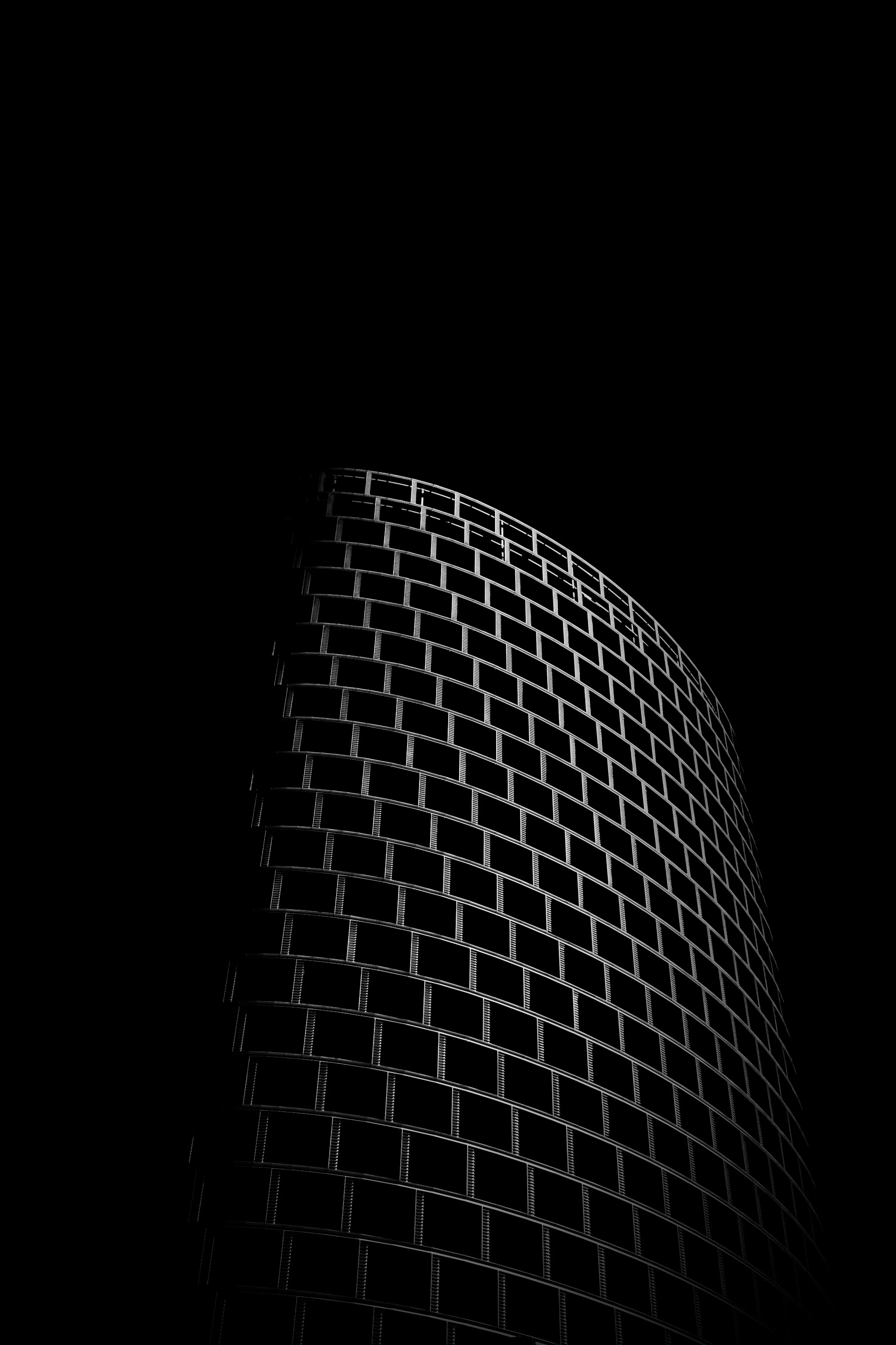 A tiled tower curves against a black sky, light grazing the grid of windows on one side and leaving the rest unlit.
