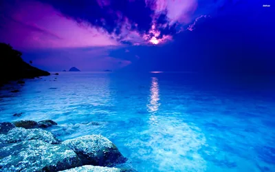 Pale rocks edge water lit an almost luminous blue, the moon breaking through violet clouds and dropping a thin reflection down the middle.