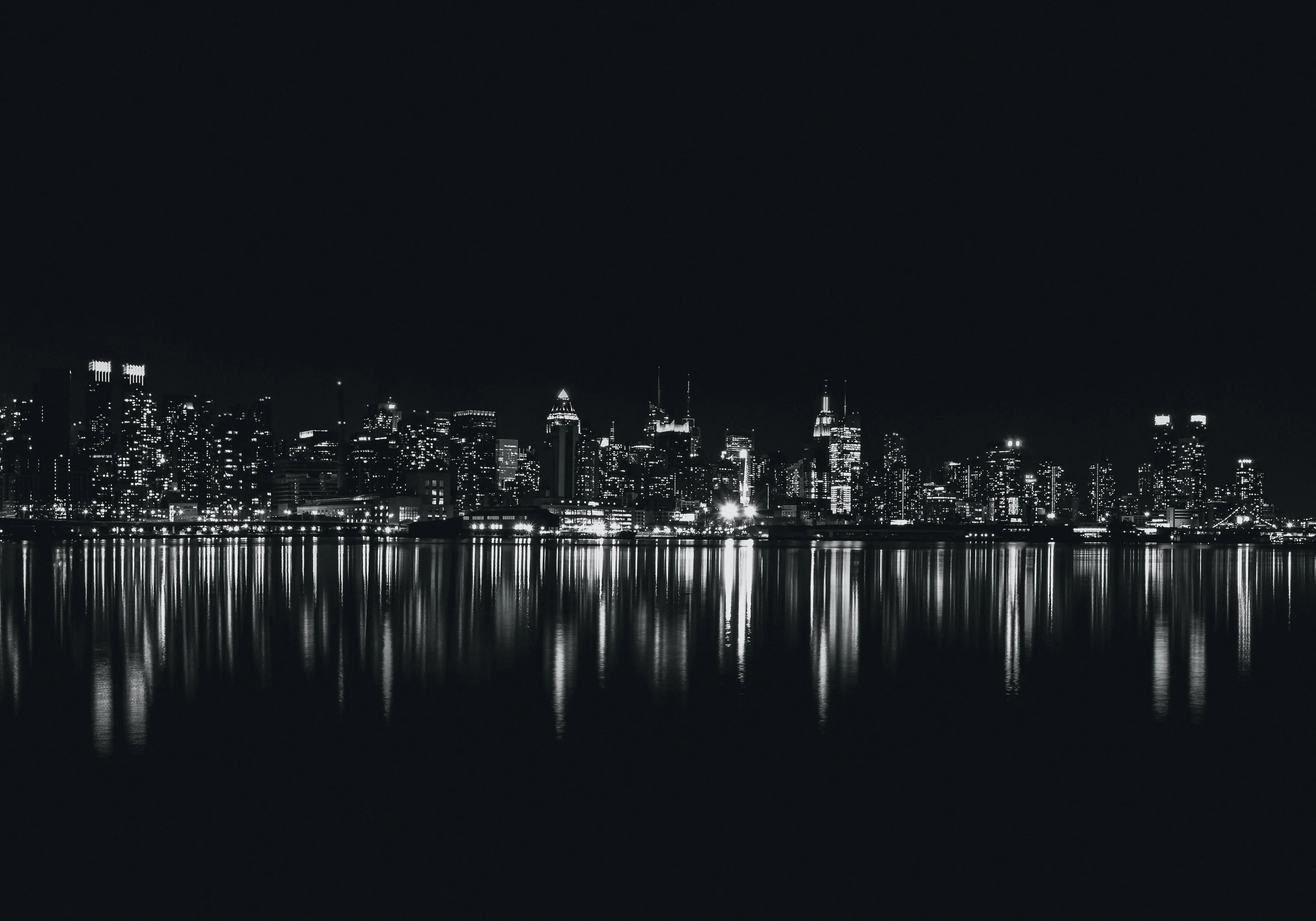 A bright band of towers burns across the middle of the frame and repeats exactly in the still water below.