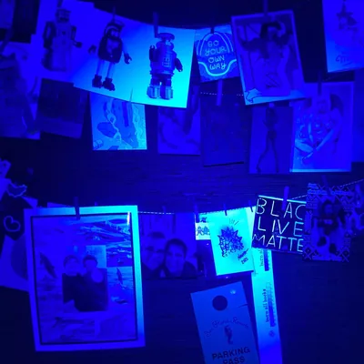 Snapshots and posters pegged to strings glow deep blue under UV light, covering the wall edge to edge with no quiet space for widgets.