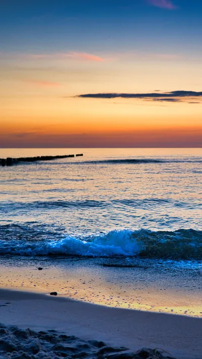 Small waves break onto wet sand under an orange afterglow, the empty upper sky fading from amber to blue for a clean status bar.