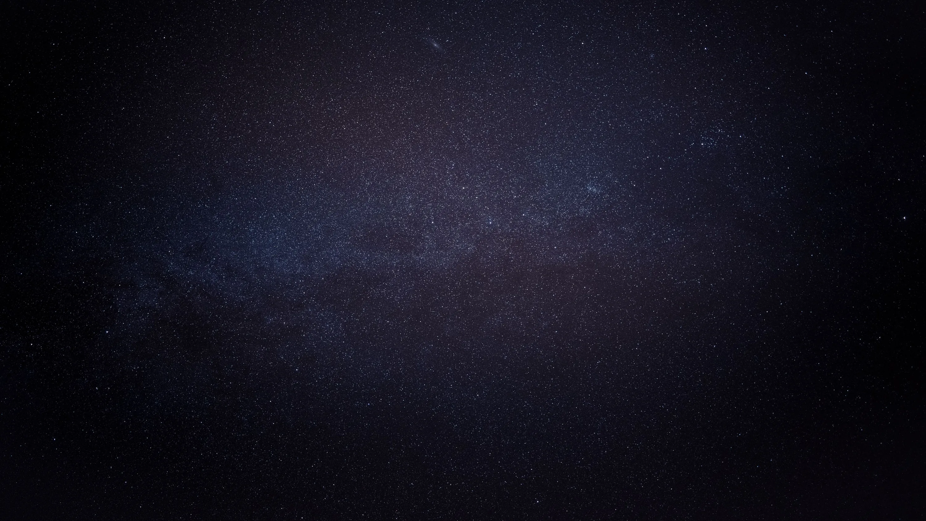 Nearly the whole frame is unbroken black, the galactic core surfacing only as a dim blue-grey blur near the centre.