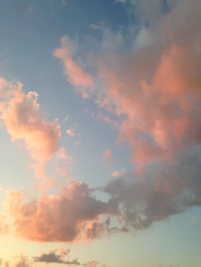 Cotton-wool clouds blushed pink by a low sun scatter across blue dusk, the colour deepest along the left edge of the frame.