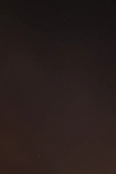 A near-empty sky in dark brown-black, only a scattering of dim stars visible — almost the whole frame is clear space.