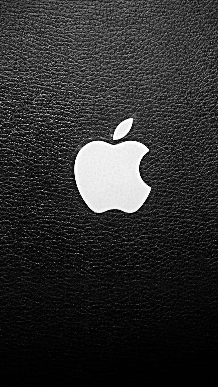 The Apple logo sits in white at the centre of grained black leather, the pebbled surface catching just enough light to show its texture.