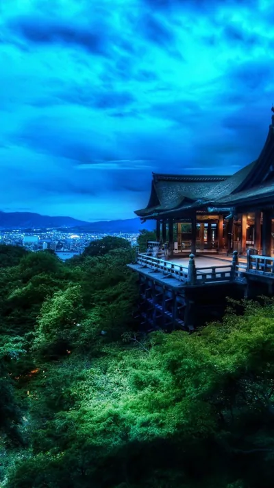 A wooden temple on tall stilts sits right of centre above dense green treetops, blue dusk clouds leaving the top of the frame dim enough for a white clock.