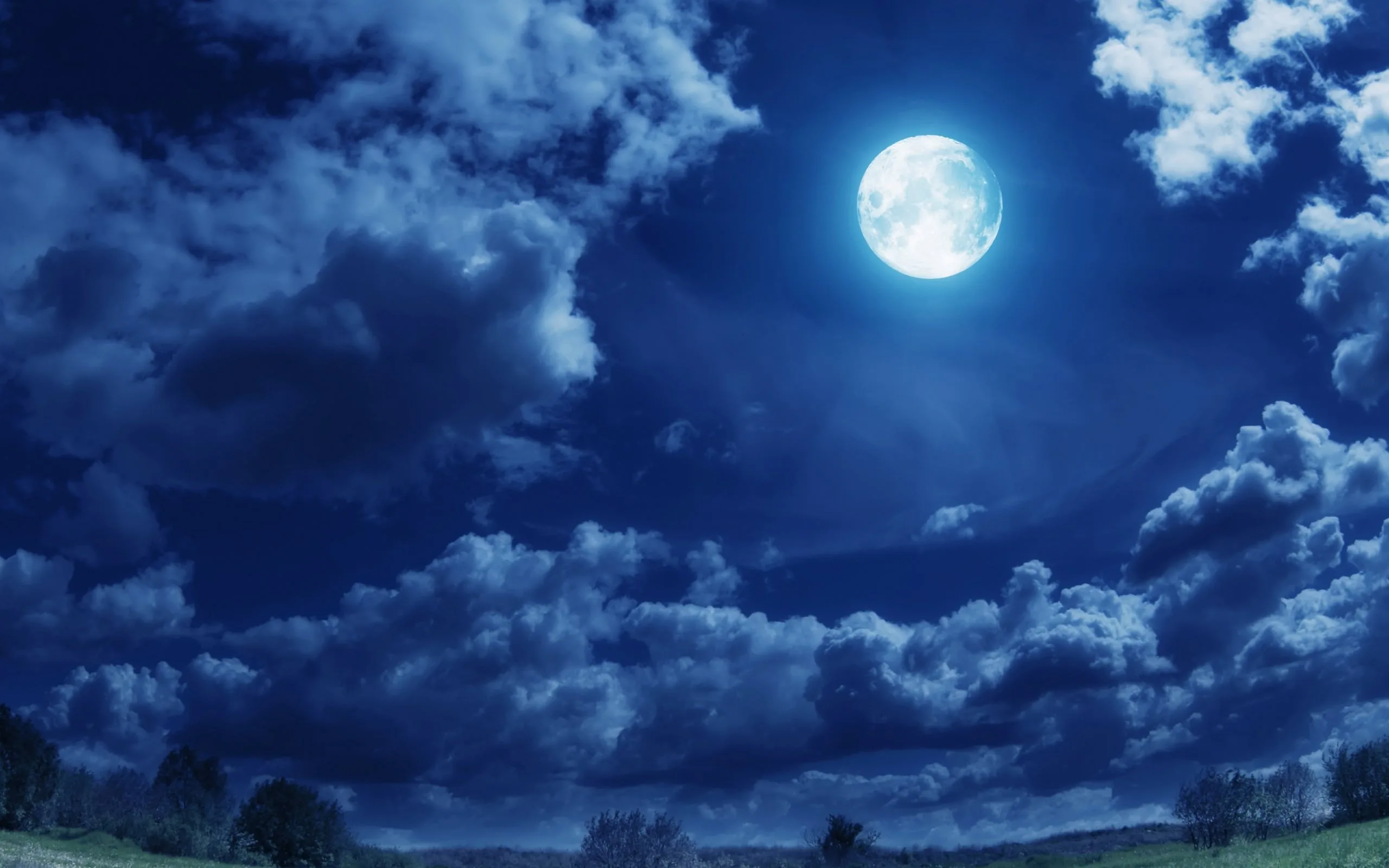 Moonlight picks out heavy blue clouds above a dark meadow and treeline, the small bright moon tucked into the top right corner.