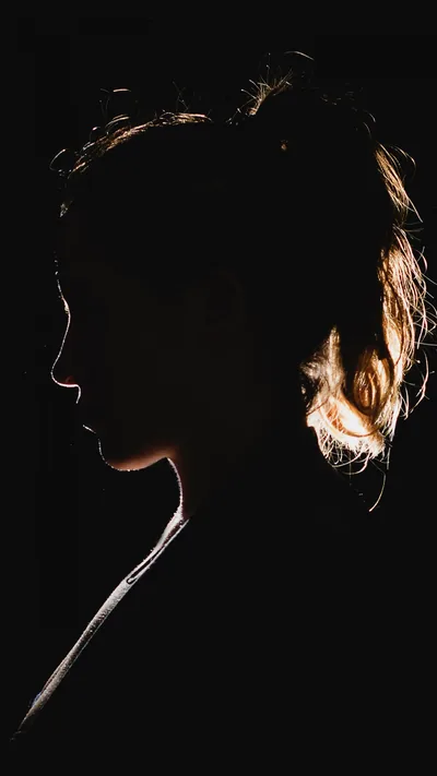 Warm light traces only the edge of a face and tied-back hair against total black, leaving nine tenths of the frame true black for OLED.