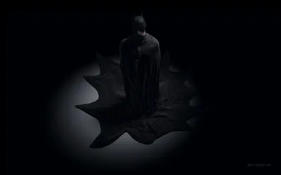 A cloaked figure stands at the centre of a glowing bat emblem, the light circling it and everything else dark.
