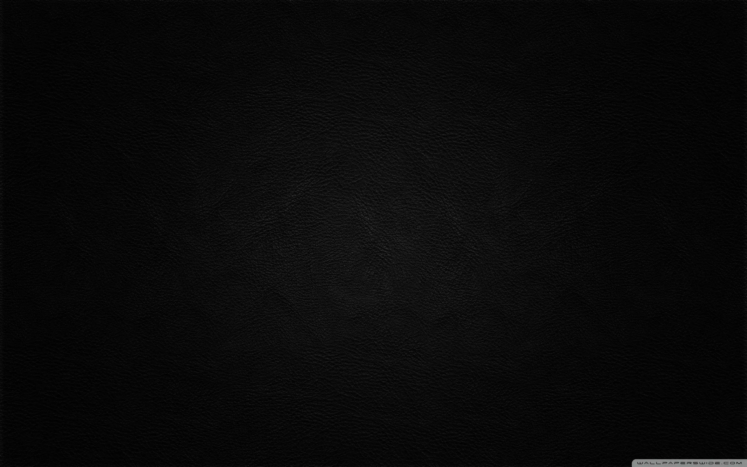 Deep black leather with the faintest circular sheen at the centre, the grain only readable where that light reaches.
