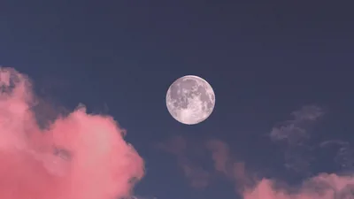 Cotton-pink clouds drift around a small full moon in a dusky blue sky, the pastel palette softer than a typical night scene.