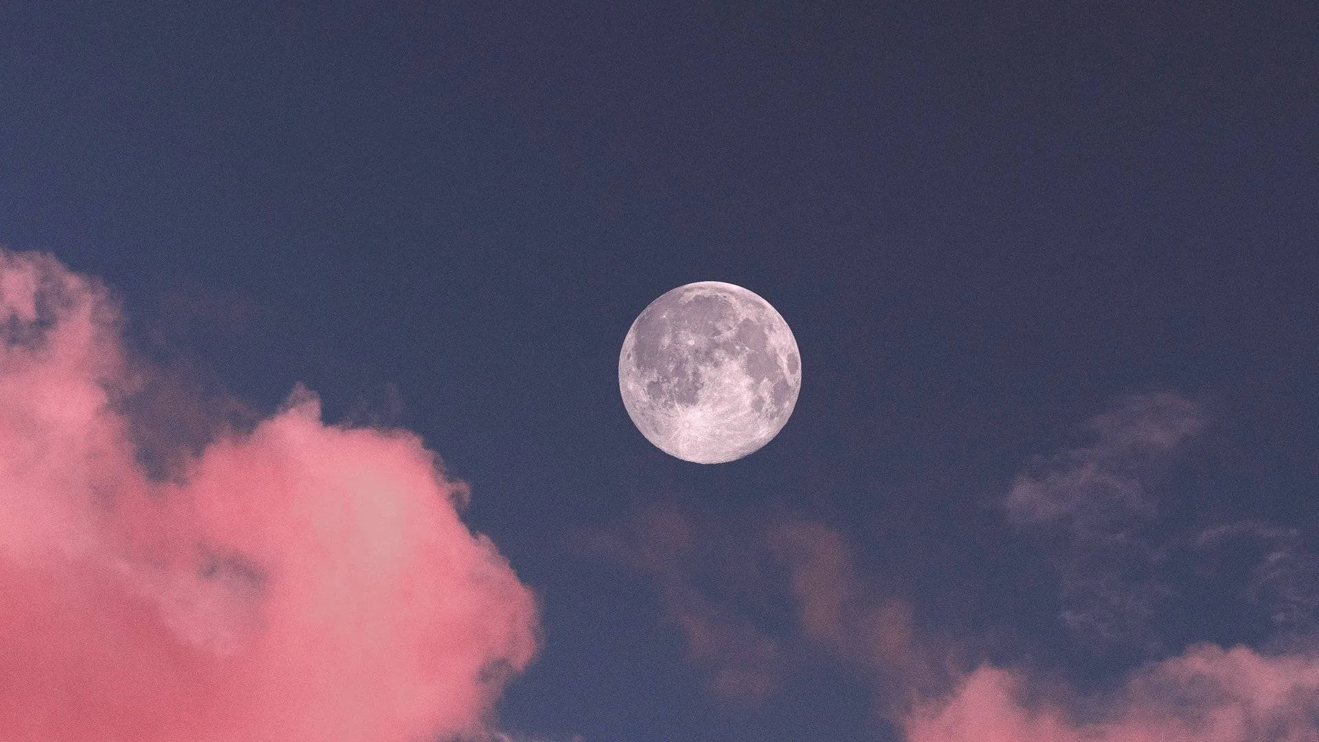 Cotton-pink clouds drift around a small full moon in a dusky blue sky, the pastel palette softer than a typical night scene.