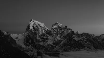 A monochrome mountain ridge rises out of a sea of cloud, the last light catching the snow while the lower slopes stay black.