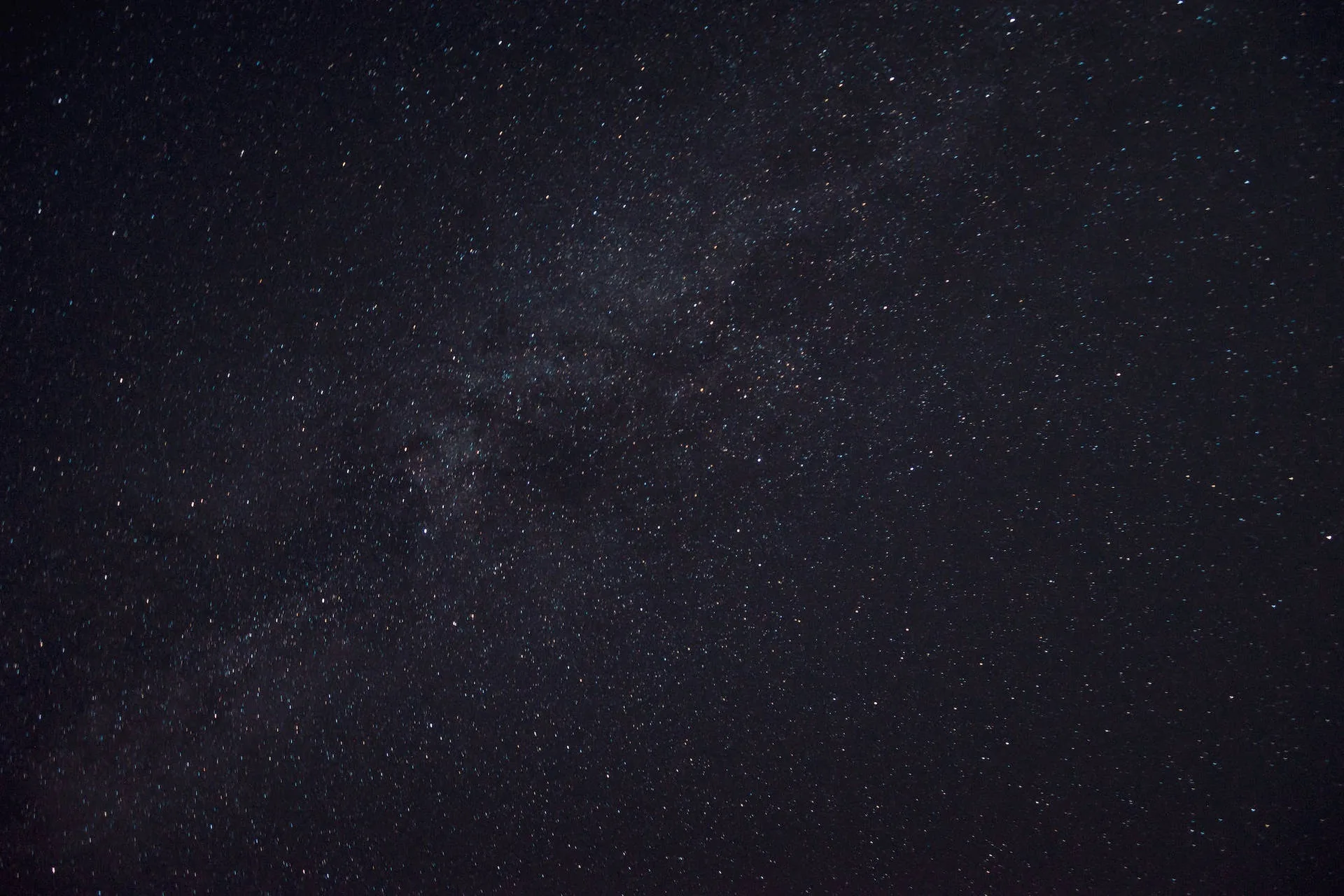 The Milky Way core spreads through a deep blue-grey sky, its dust clouds soft and unfocused with brighter stars punching through.