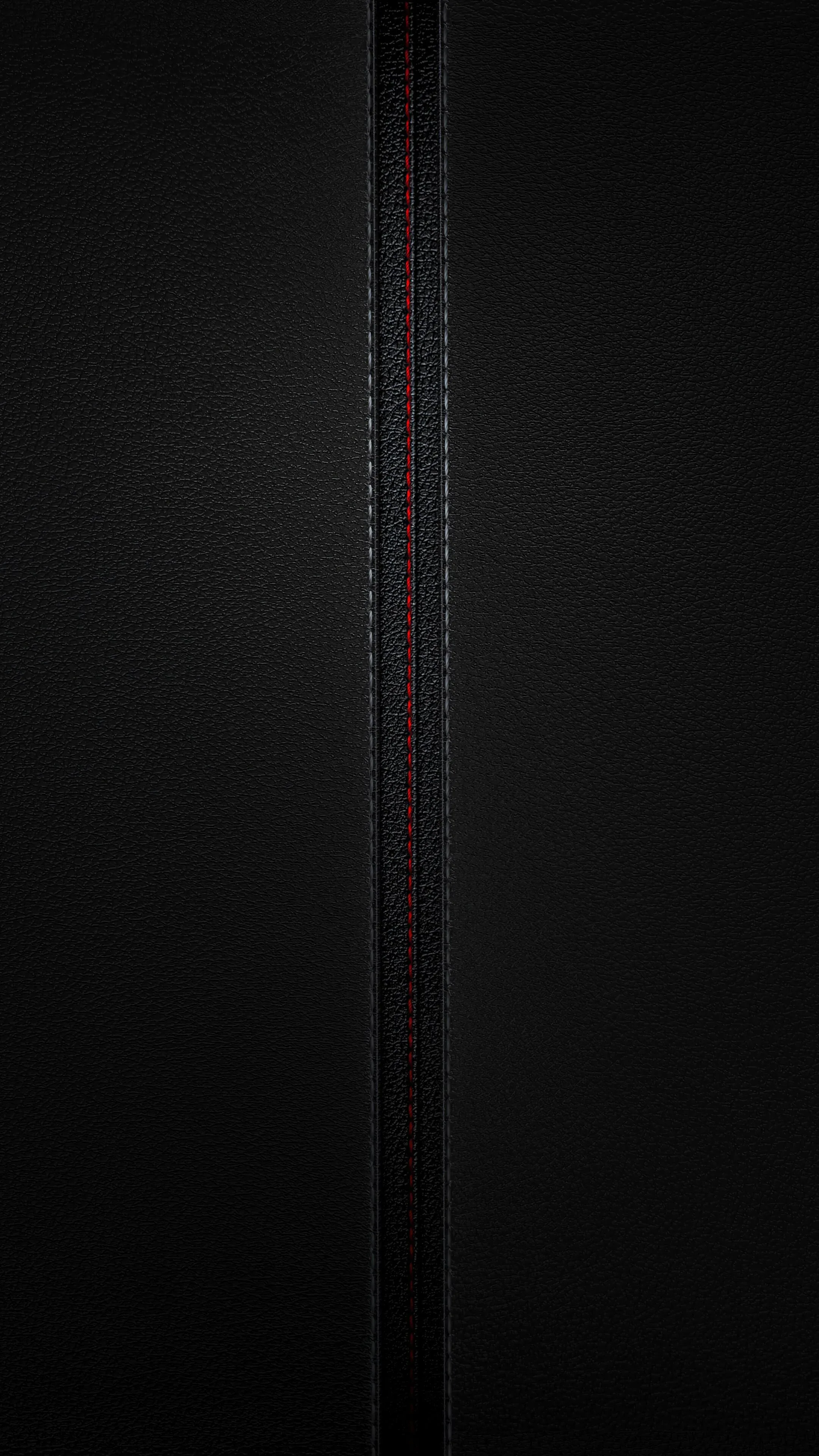 Fine-grain black leather split down the middle by a stitched seam, red thread just catching the light.