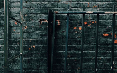Dark green-painted brick sits behind a black metal railing, patches of orange rust showing where the paint has flaked away.