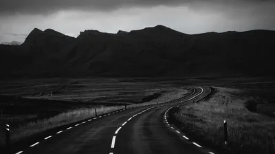 A road curves away through open moorland toward a dark ridge, marker posts running along both verges.
