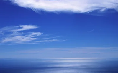 A minimalist seascape in nothing but blues, one white cloud along the top and a strip of sun glint where sea meets sky.