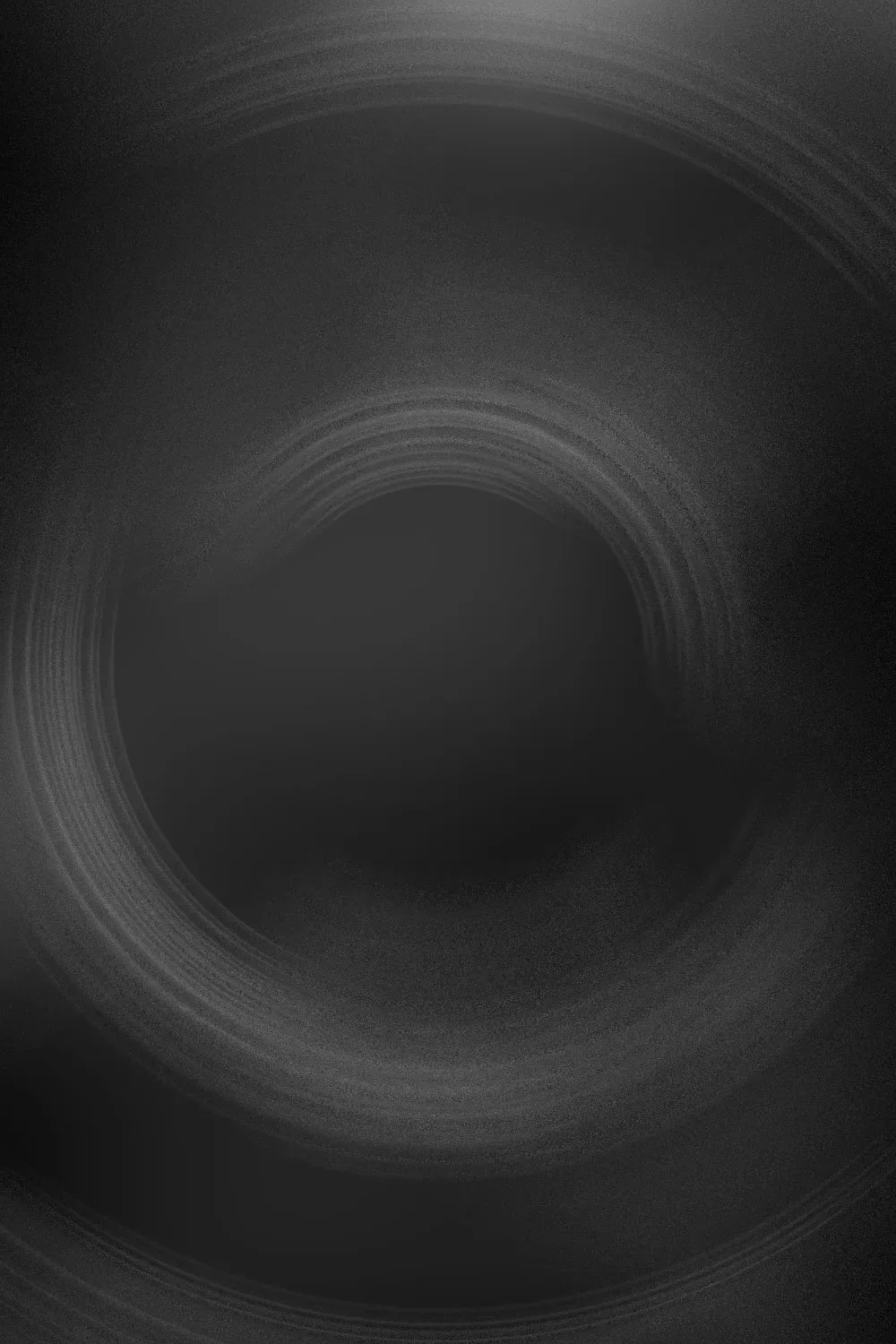 Concentric smears of grey spin out from a hollow centre in a slow motion blur, the corners falling away to near-black in a heavy vignette.
