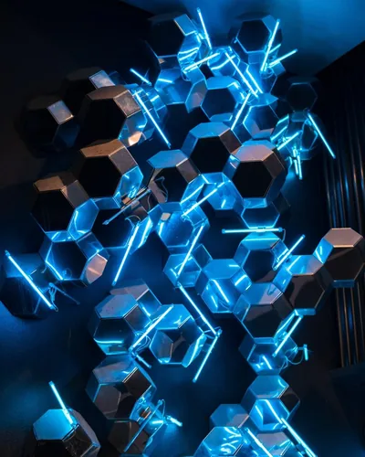 Mirrored hexagonal blocks climb a dark wall, cyan tube lights threaded between them, with the glow strongest along the middle column of this portrait frame.