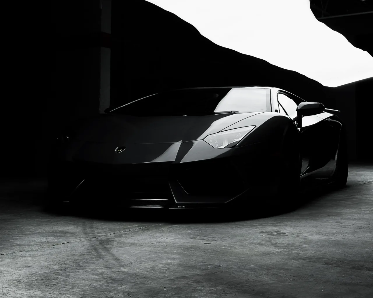 A black Lamborghini waits nose-out in an unlit garage, daylight from the right picking out only the fender line — everything above the roof is pure black.
