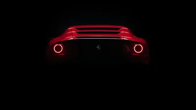 Two round red lamps and a slatted rear deck are all that reads, the prancing horse badge just visible between them on an otherwise unlit body.