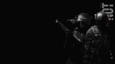 Two figures in tactical gear move through darkness with a rifle raised, one hard light catching their helmets while the left half of the frame stays empty.