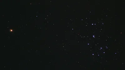 A loose blue star cluster sits to the right of the frame while a single orange-red star burns alone on the left, the space between them almost empty.