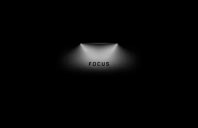 A single word sits under a narrow cone of light on a black wall, everything outside the beam left dark.