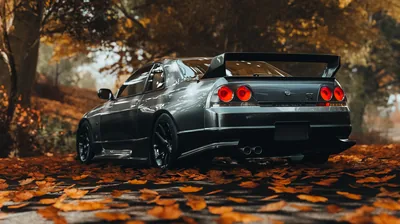 Rear three-quarter of a grey R33 on a forest road, big rear wing up and orange leaves drifted across the tarmac under the diffuser.