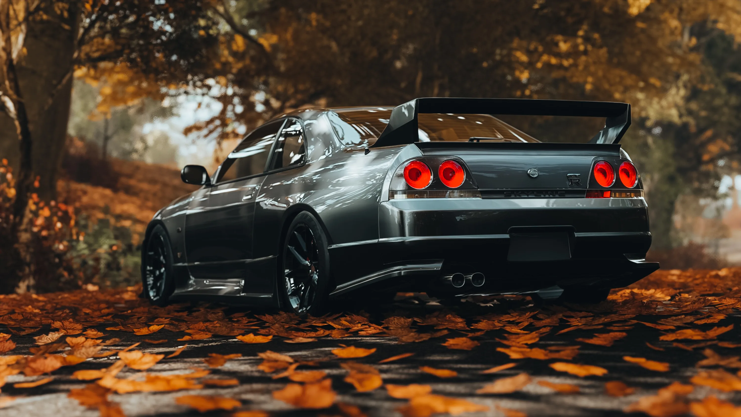 Rear three-quarter of a grey R33 on a forest road, big rear wing up and orange leaves drifted across the tarmac under the diffuser.