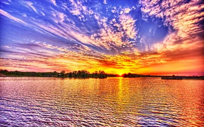 An HDR sunset saturates every cloud band in orange, pink and blue above a lake, the ripples carrying the colour down the frame.