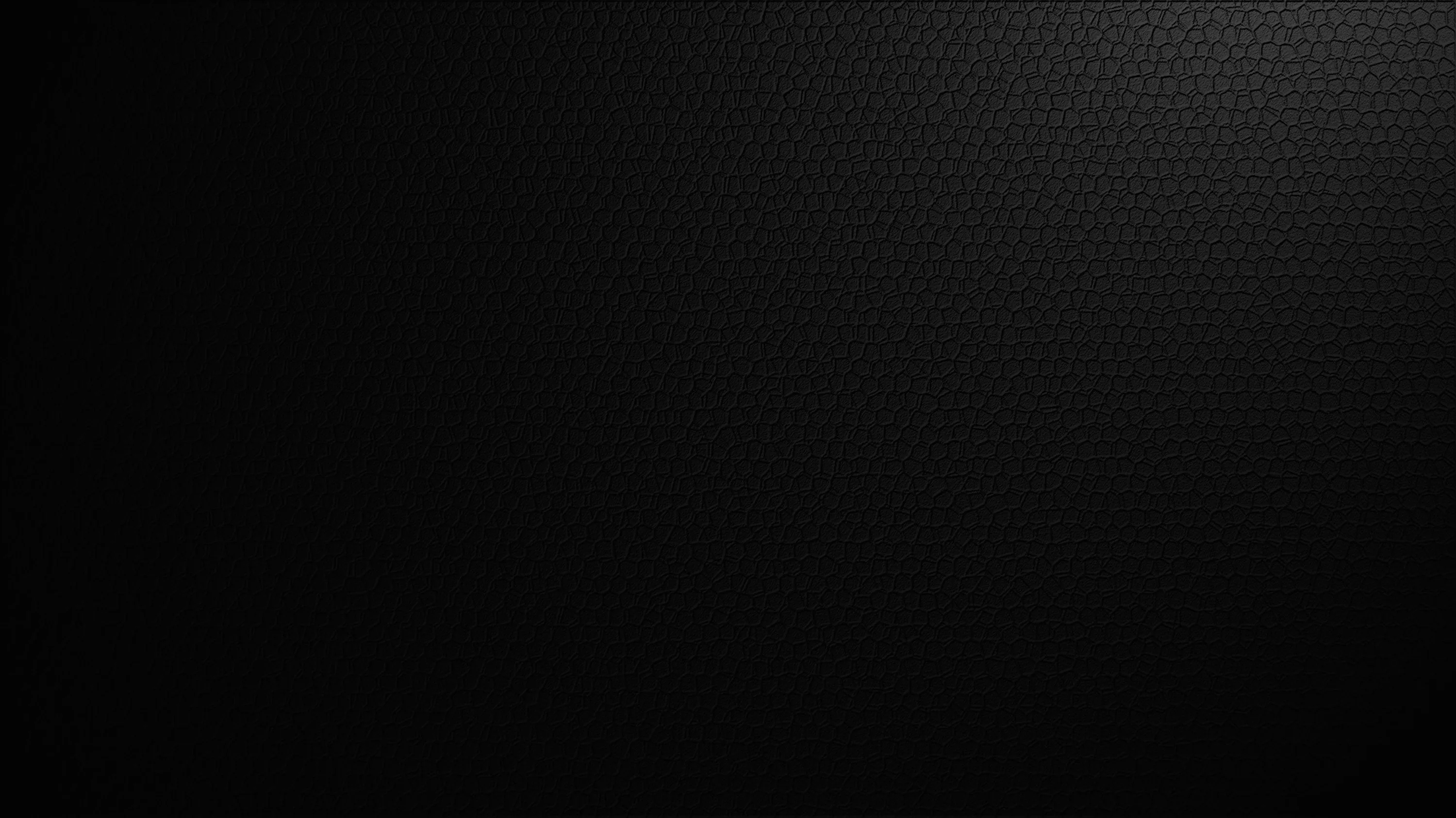A tight carbon fibre weave fills the frame, the pattern picked up by faint light from the left while the right side drops into flat black.