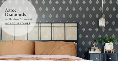 A charcoal wall papered in small cream diamonds sits behind a black metal bed, with a brass pendant lamp hanging on the right.