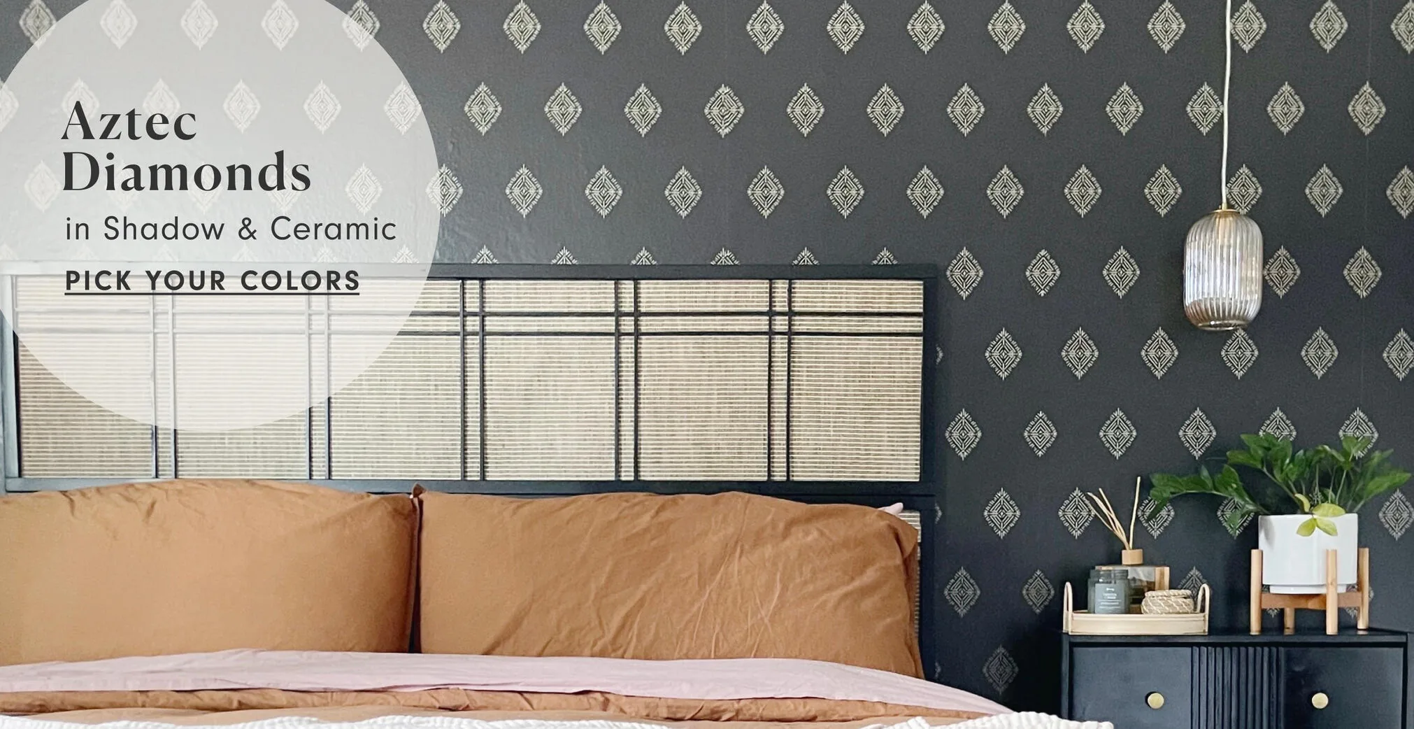 A charcoal wall papered in small cream diamonds sits behind a black metal bed, with a brass pendant lamp hanging on the right.