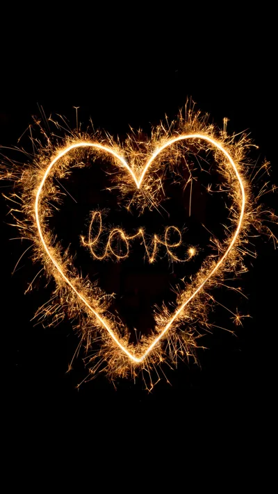 A heart traced in the air with a sparkler, the word love looped in the middle, orange embers scattering into the black around it.