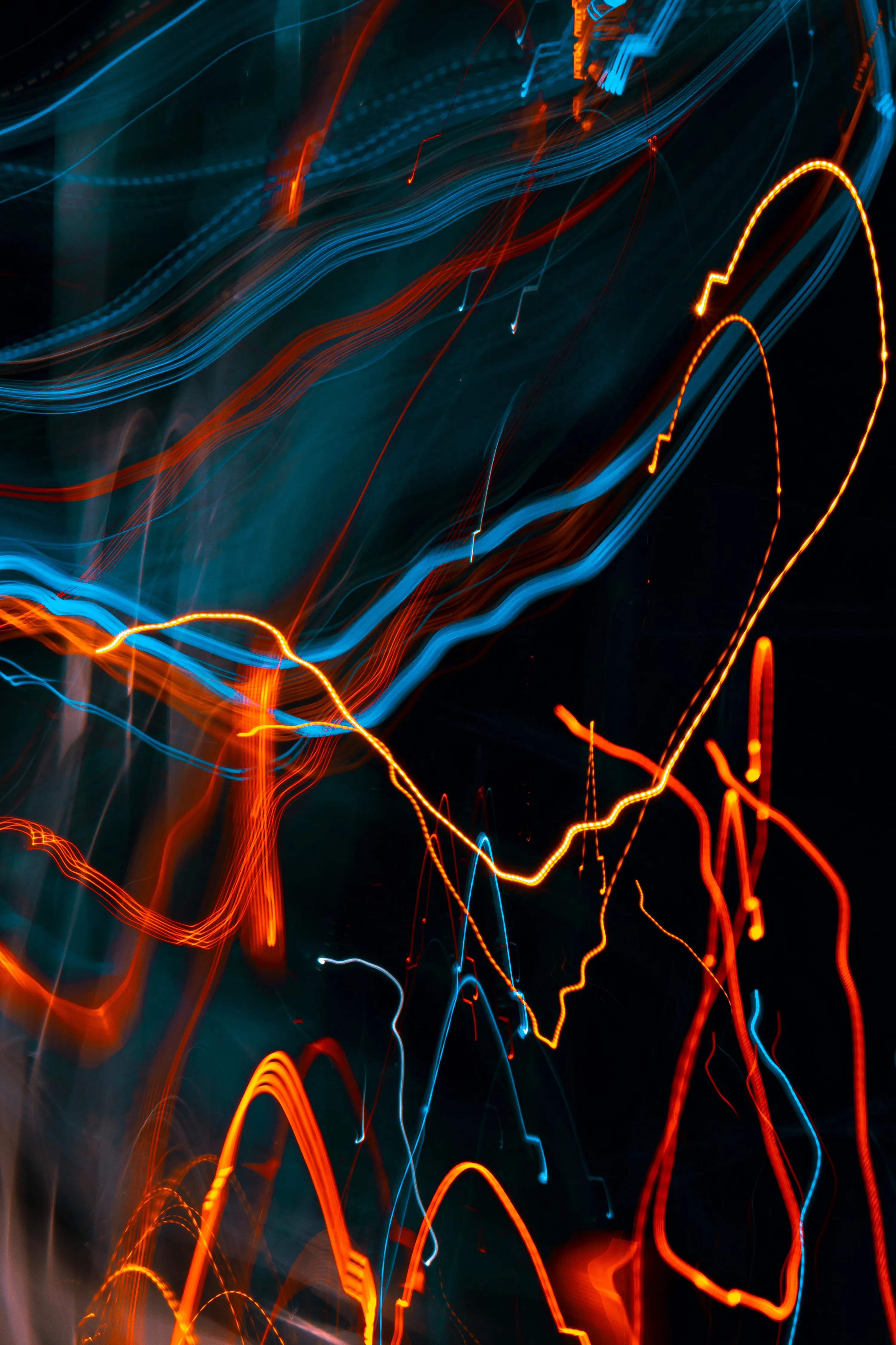 Long-exposure light trails in orange, blue and yellow whip across the dark — an abstract that hides a notch and status bar equally well.