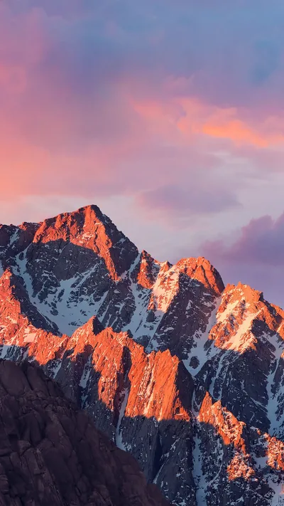 First light turns craggy snow-lined ridges copper against soft pink clouds, the shadowed rock in the lower left offering the calmest spot for widgets.