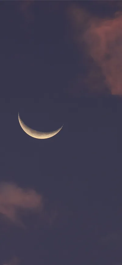 A thin crescent hangs left of centre in a mauve dusk, soft clouds catching the last light in the top and bottom corners.