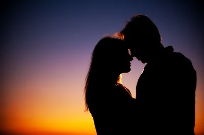 Two darkened figures lean in close, framed against a sky that runs from deep blue overhead to burnt orange along the horizon.
