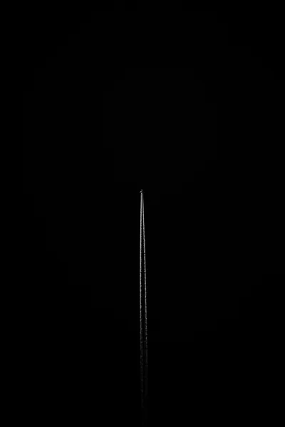 A single slender spire rises out of pitch black, its edge just catching enough light to separate from the background.