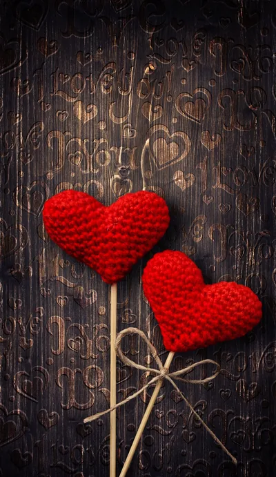 Two crocheted hearts on wooden sticks lie tied with twine across worn dark planks, hearts faintly carved into the grain behind them.