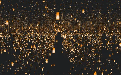 Hundreds of warm paper lanterns hang and repeat into mirrored darkness, a lone silhouette standing among them at the centre.