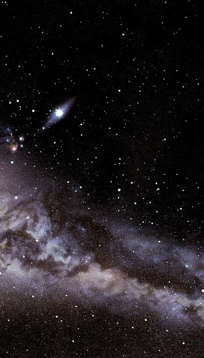 One star flares near the top of a crowded black sky while the pale galactic band spreads across the lower half in brown and grey dust.